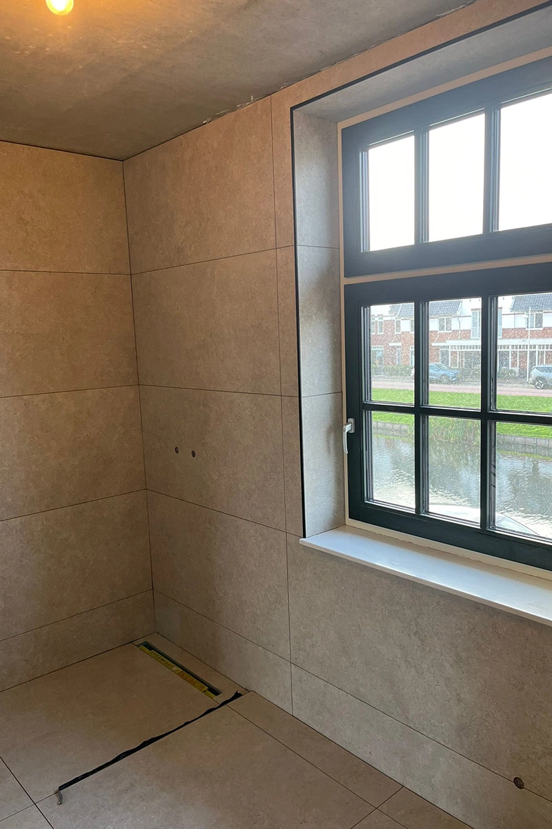 Strakke betegeling met grijze wand- en vloertegels (120x60 en 90x90 cm) en afschot naar drain in badkamer, uitgevoerd door Roy van den Bosch – VDB Tegelwerk.