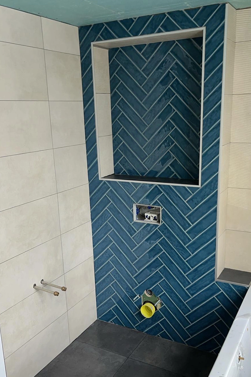 Toilet met blauwe visgraat wand en lichte, strak afgewerkte wandtegels, in combinatie met donkere moderne vloer tegels - tegelwerk door VDB Tegelwerk.
