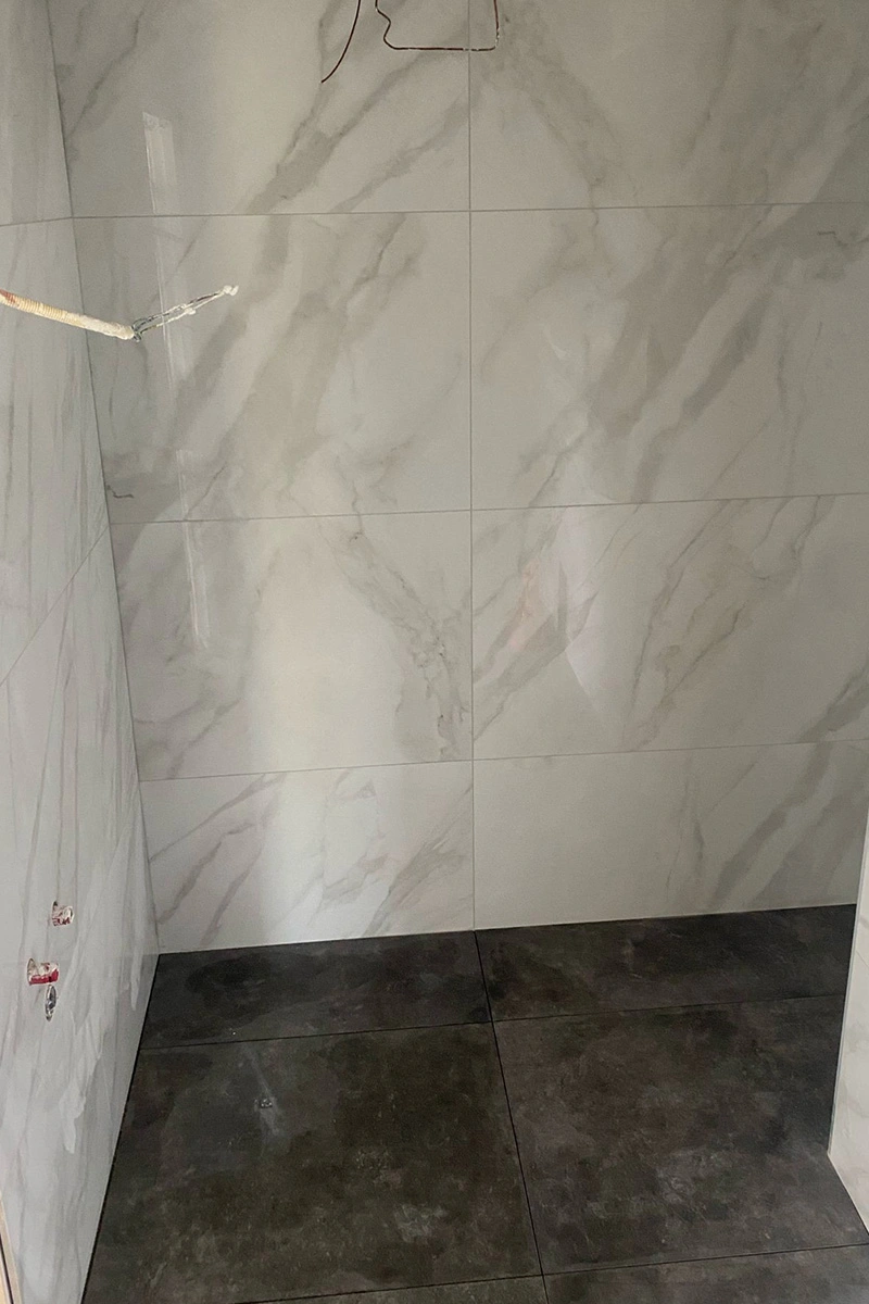 Badkamer met wit-grijze marmerlook wandtegels van 120x90 cm, gecombineerd met een donkere 90x90 cm vloertegel. Afwerking door VDB Tegelwerk.