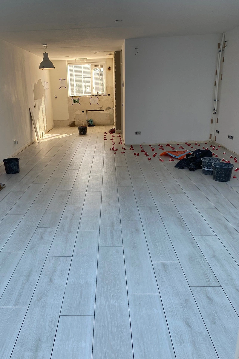 Lichte houtlook tegelvloer in woonkamer, gelegd met behulp van een levelingssysteem, zichtbaar in de hoek van de ruimte. Uitgevoerd door VDB Tegelwerk.