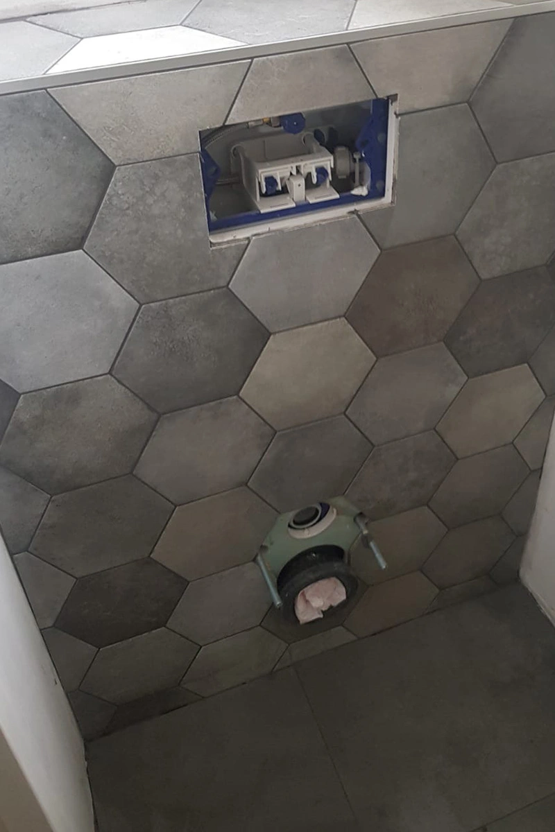 Modern donker toilet met strakke donkere vloertegels en hexagon wandtegels achter het toilet. Tegelwerk verzorgd door VDB Tegelwerk.