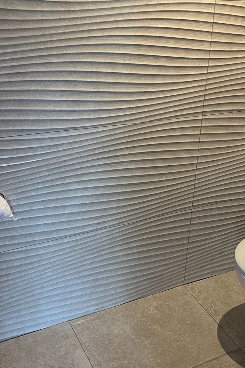 Modern grijs toilet met speciale wandtegels in golfpatroon en reliëfstructuur. Tegelwerk door VDB Tegelwerk.