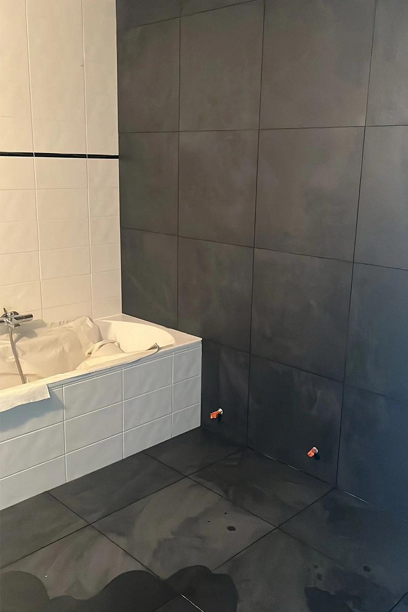 Moderne badkamer met ligbad, witte wandtegels met zwarte accentstreep, en strakke zwarte vloer en wandtegels voor een stijlvol contrast. Uitgevoerd door VDB Tegelwerk