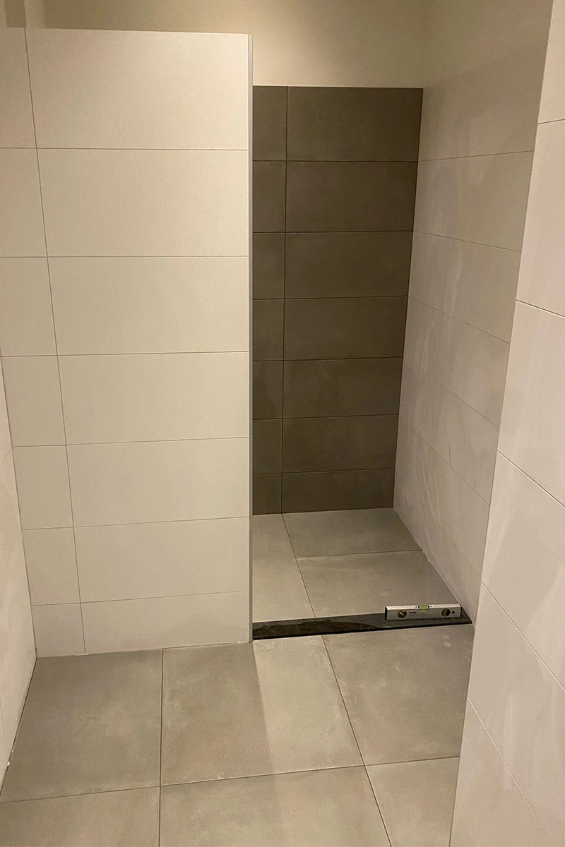 Lichte badkamer met moderne vloertegels en een natuurstenen dorpel, verschillende grijstinten en douche wand, verzorgd door VDB Tegelwerk.