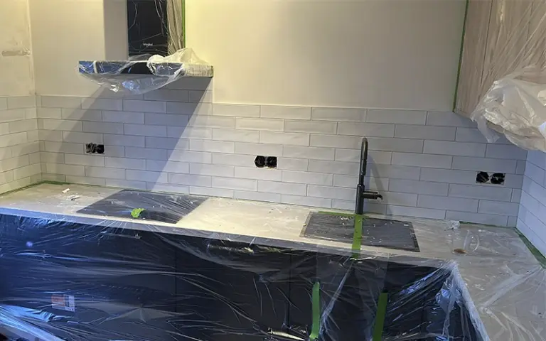 Spatwand L-keuken met witte tegels halfsteens bij inductiekookplaat en gootsteen in Amsterdam.