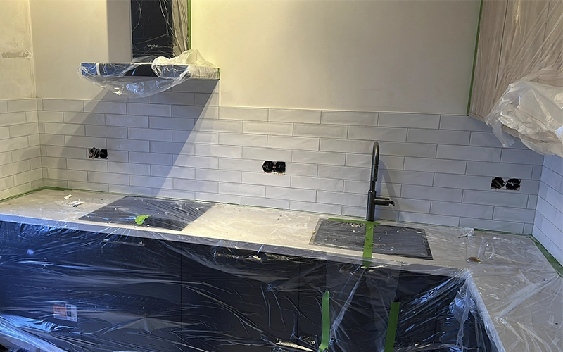 Spatwand L-keuken met witte tegels halfsteens bij inductiekookplaat en gootsteen in Amsterdam.